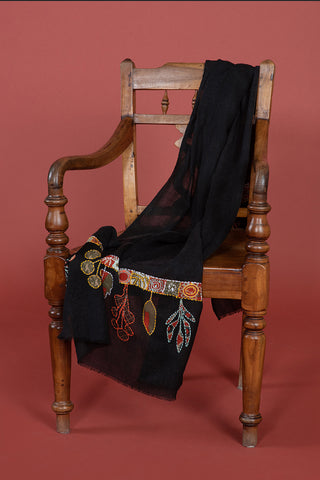 A black scarf with orange and brown leaf patterns, draped across a chair.