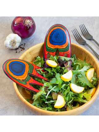 A pair of colorfully painted bamboo salad servers that look like hands, in a bowl of salad.