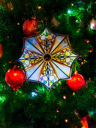 An ocatagonal stained glass ornament with a floral design, hanging from a holiday tree.