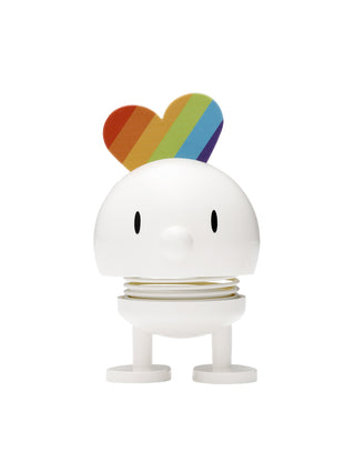 A smiling white figure with a spherical head and spring in its middle, with rainbow attached to the back of its head.