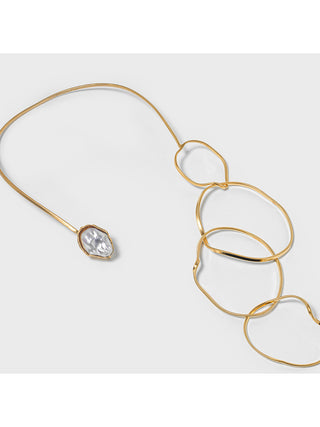 Angled view of a brass collar necklace with a mother of pearl piece on the left and four loops dangling down on the right.