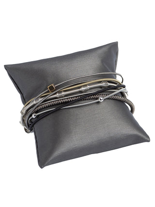 A bracelet with muticolored wire bands and bead, wrapped around a grey pillow.
