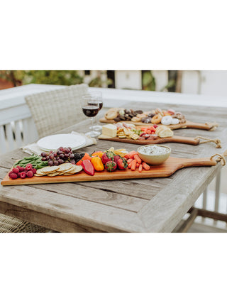 Three long wooden planks covered with food on a wooden table, wine glasses in the background.