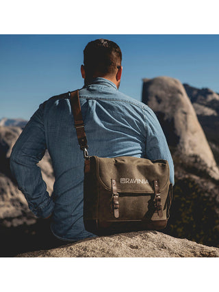 A man outdoors in a rocky area, with a tote slung over his shoulder, RAVINIA printed on it in white.