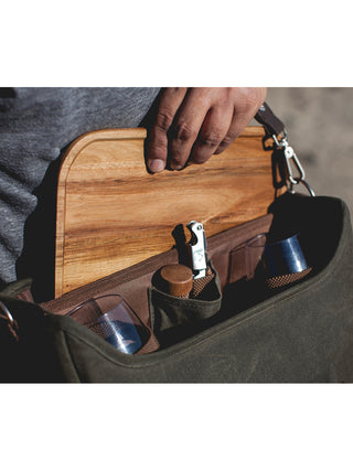 An open canvas bag with a hand holding a wooden mini table in front of partially concealed wine bottles and a corkscrew.