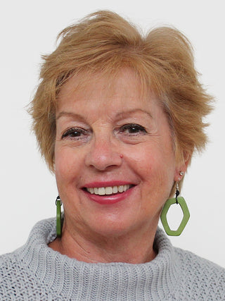 Angled view of earrings made of aa vibrant lime green wooden link, on a smiling model looking directly ahead.