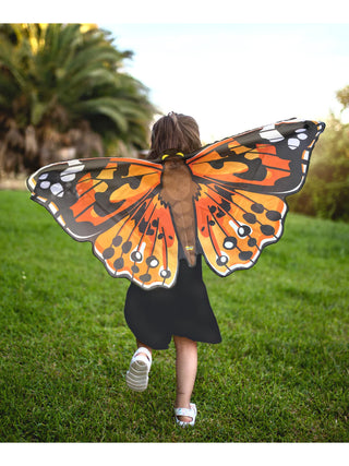A young girl from the back, running, with a 4-foot wide orange and black polyester butterfly attached to her.