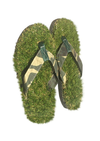 A pair of flip flops that appear to be made of grass, with camoflaged straps, against a white background.