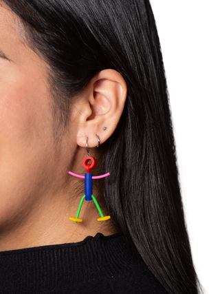 Close-up of a young woman's ear with a colorful earring of a little stick figure man.