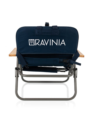 The back of a navy padded foldable chair with wooden arm rests, branded with the Ravinia logo in white.
