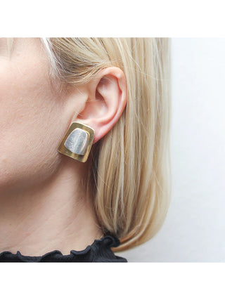 An earring of lightly dished brass tapered rectangle layered with a silver-toned, domed tapered rectangle, on a blond-haired model's ear.