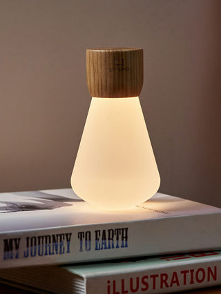 An illuminate light bult with a wooden base, upside down, on top of books.