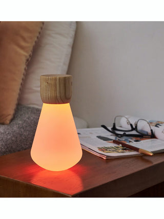 An upside down light bulb, illumniated in orange, with a wooden base, on top of a desk.