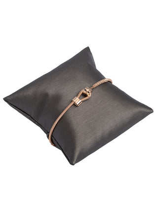 A gold bass string bracelet with its loop in front, wrapped around a small grey pillow.