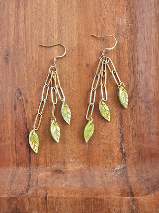 A pair of gold earrings with 3 chains, each ending in a green leaf.