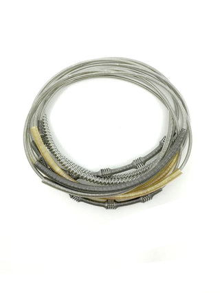 A multi-strand, multi-colored piano wire bracelet in tones of silver, gray and gold.