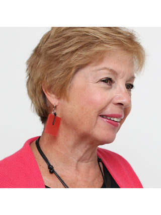 A pair of translucent blue, rectangular earrings with silver-toned hooks, on a smiling model.