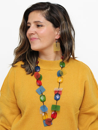 A colorful resin bead necklace, flat, with a variety of shapes and colors., on a smiling model in a yellow top.