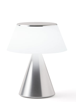 A lamp with a triangular aluminum base and an illuminated white shade.