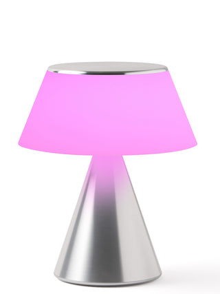 A lamp with a triangular aluminum base and an illuminated  fuchsia shade.a