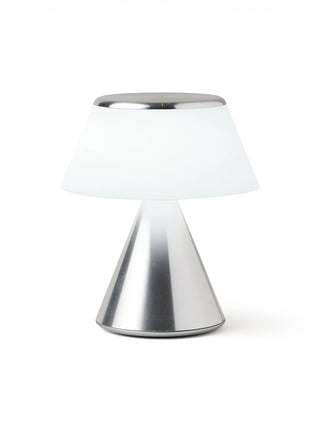 A lamp with a triangular aluminum base and an illuminated  white shade.