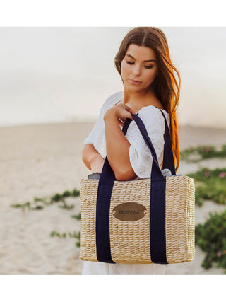 A woman at the beach with a picnic basket tote slung over her shoulder, a round Ravinia logo in its center.