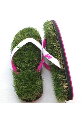 A pair of flip flops that appear to be made of grass, with pinks and white straps, against a white background. The left is flat, the other on its side.
