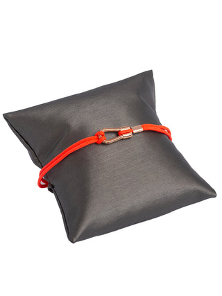 A pink string bracelet with a gold loop, around a small grey pillow.