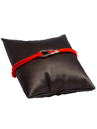 A pink cord bracelet with a silver loop, styled around a small grey pillow.