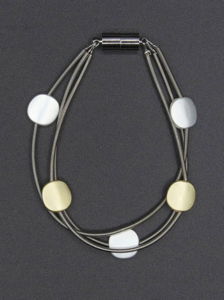 A three-strand piano wire bracelet, flat, with gold and silver-toned discs and a silver-toned magnetic clasp.