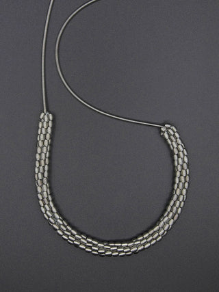 Long Silver Piano Wire Necklace with Woven Silver Beads, flat on a gray background.
