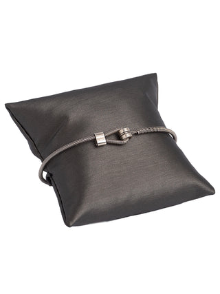 A silver bass string bracelet with its loop in front, wrapped around a small pillow.