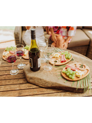 A table with a bottle of wine, two full and two empty glasses, and fur oval trays, all filled with appetizers like grapes, cheese and meat.