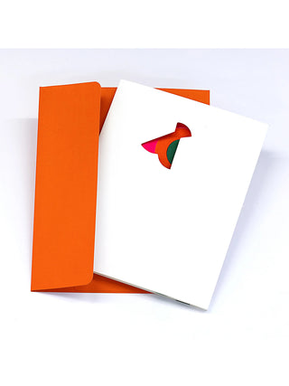 A white greeting card with an insect-like cutout in the center, in front of an orange envelope.