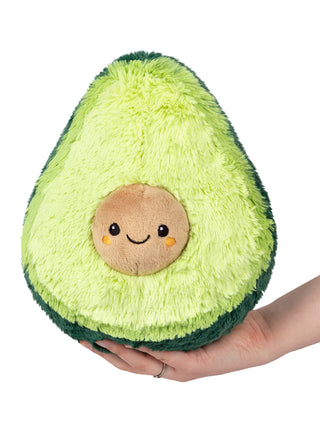 A plush version of an avocado, with its pit a smiling face, held up by a hand.