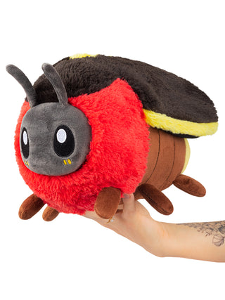 A large red, black and yellow plush firefly being held up by a hand.