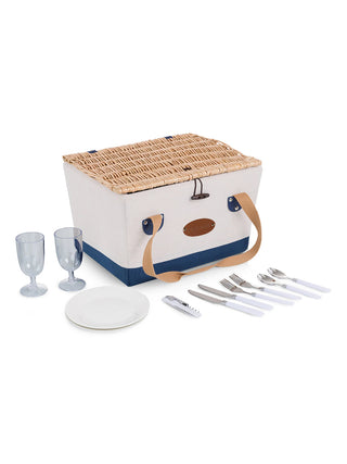 A canvas picnic basket with its contents — two plates, two wine glasses, two sets of cutlery, and a corkscrew — laid around it.