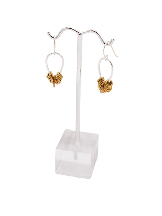 A pair of silver teardrop earrings with small brass rings on each, hanging on a silver earring stand.