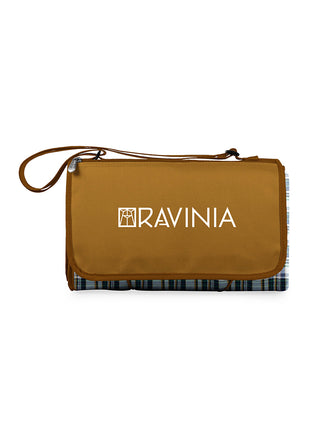 A beige and English plaid blanket tote with the Ravinia logo, folded to show its portable tote form and the adjustable shoulder strap.