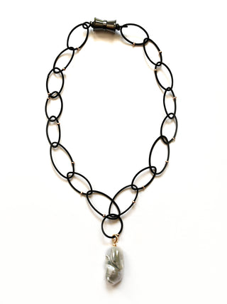 A black ring necklace with tiny gold beads and a large faul-pearl pendant at the bottom.