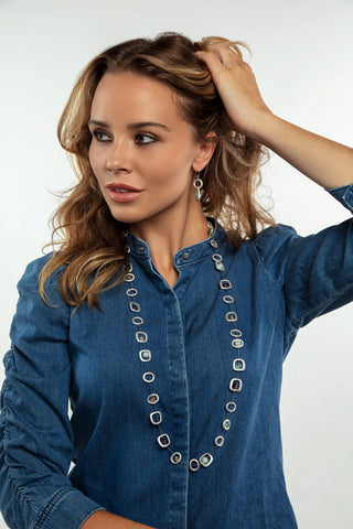 A model in a blue denim shirt wearing a silver-toned geo necklace.