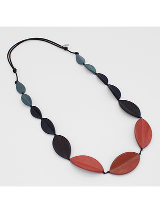An angled view of a necklace with wood beads in warm spice tones in rust, dark brown and gray are hand strung in size order on an adjustable black wax cord. The slight curve of each beads gives a dimensional feel to the necklace.
