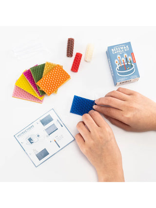 A pair of hands working with a blue wax square, with several other colored wax squares off to the left. A box called Beeswax Candle Kit is in the upper right.