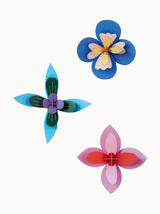 Three colorful paper flowers on a wall, the top two mainly cobalt, and the bottom one red and pink.