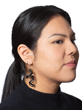 A pair of black plastic earrings with a swirling pattern, on a woman with black hair and a black top.