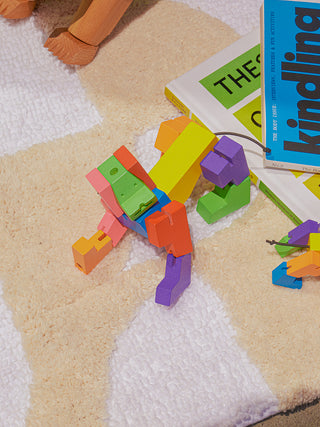 A multicolored robot dog on a carpet, looking up, next to some magazines.