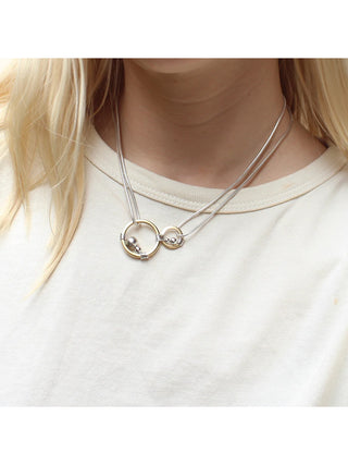 On a woman's neck, a necklace with two thick rings in brass with silver beads and wire wrapping, hung on two doubled strands of silver snake chain.