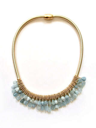A necklace made of thick, gold-toned piano wire with two tiers of aquamarine-colored stones hanging from it.