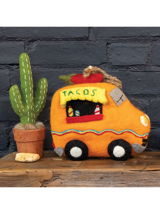 An orange felt birdhouse that looks like a taco truck, sitting on a shelf next to a felt cactus.