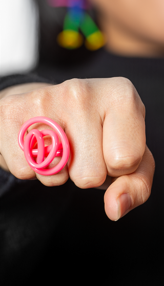 A pink squiggle ring on a finger.